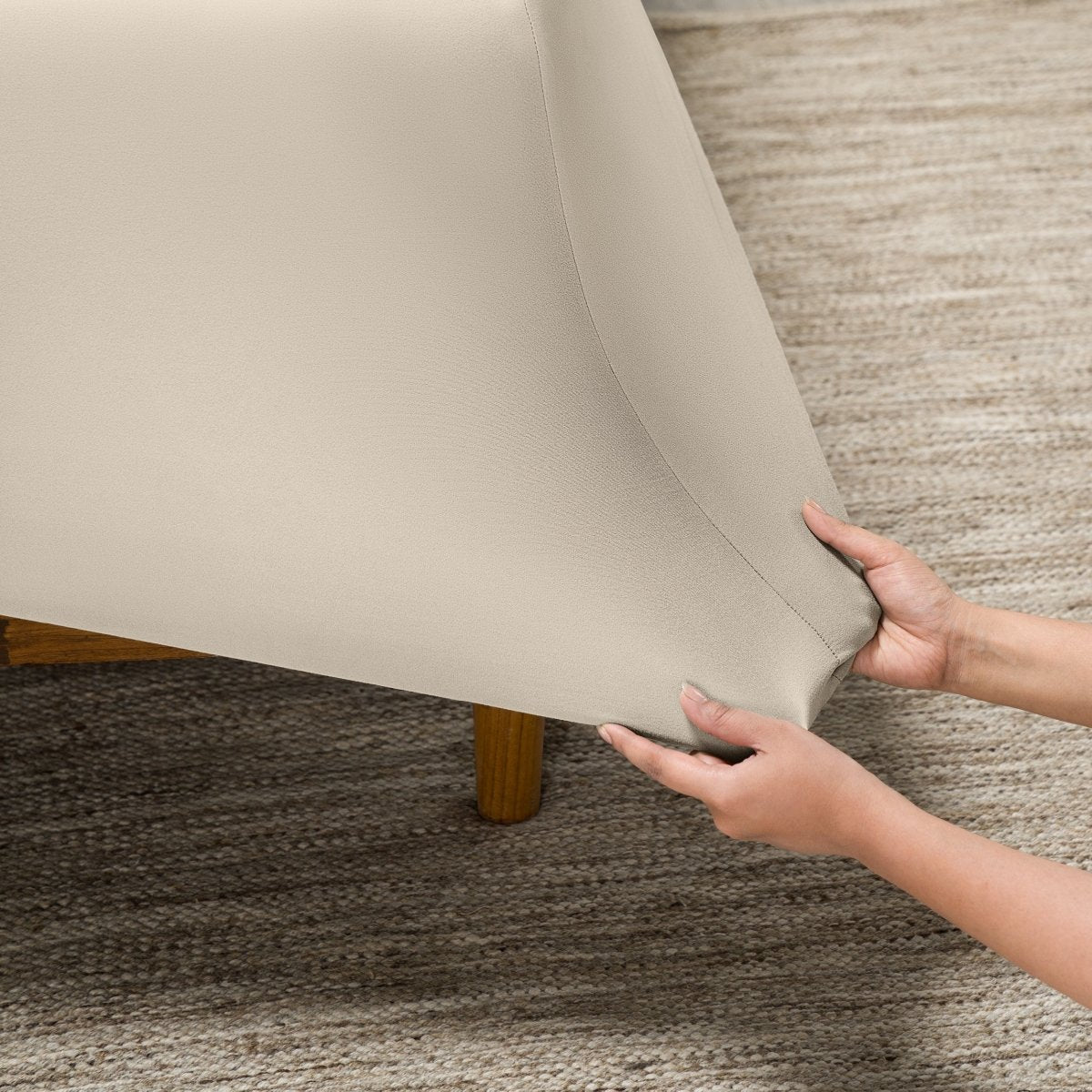 Person putting a fitted sheet on a bed on carpeted floor.