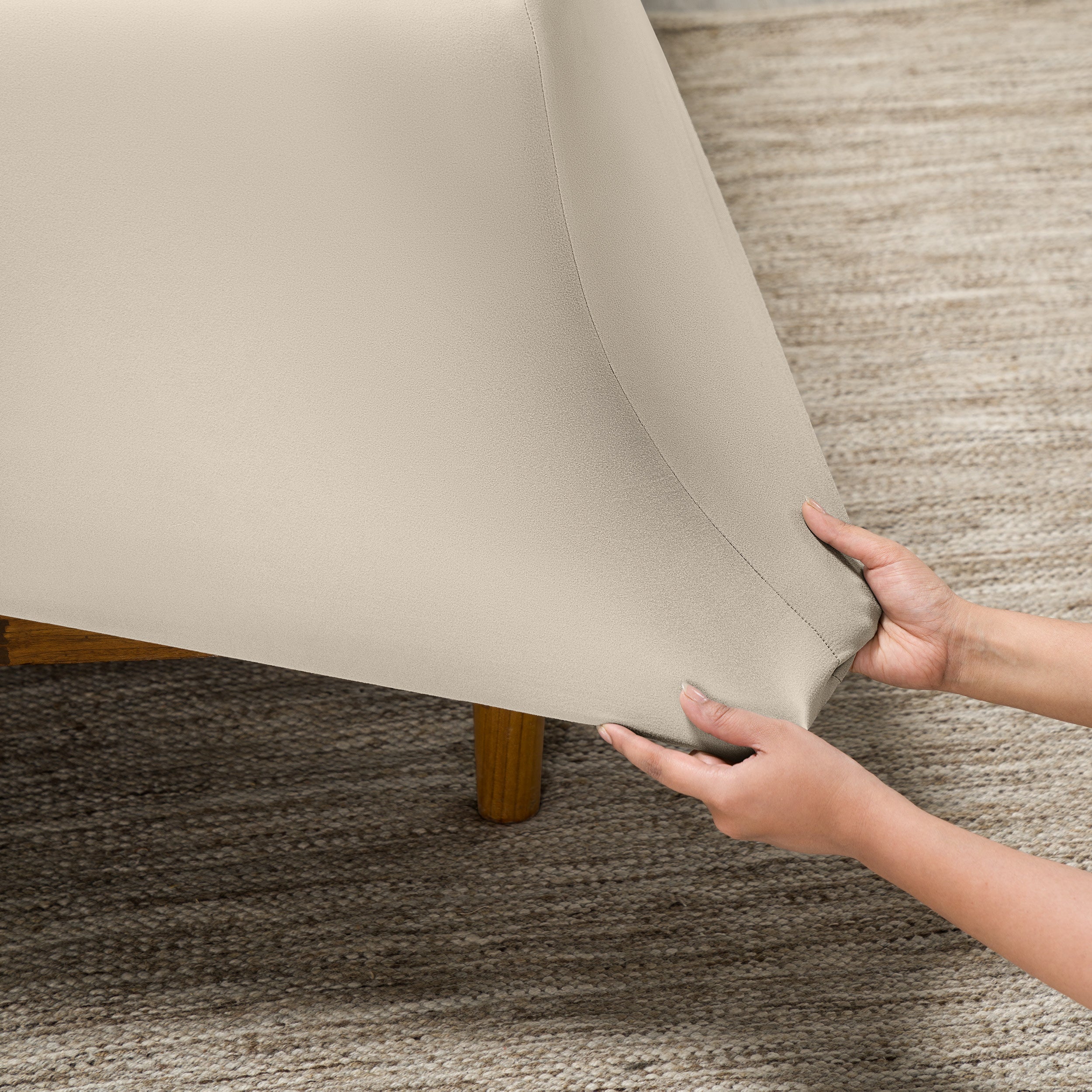 Person putting a fitted sheet on a bed on carpeted floor.