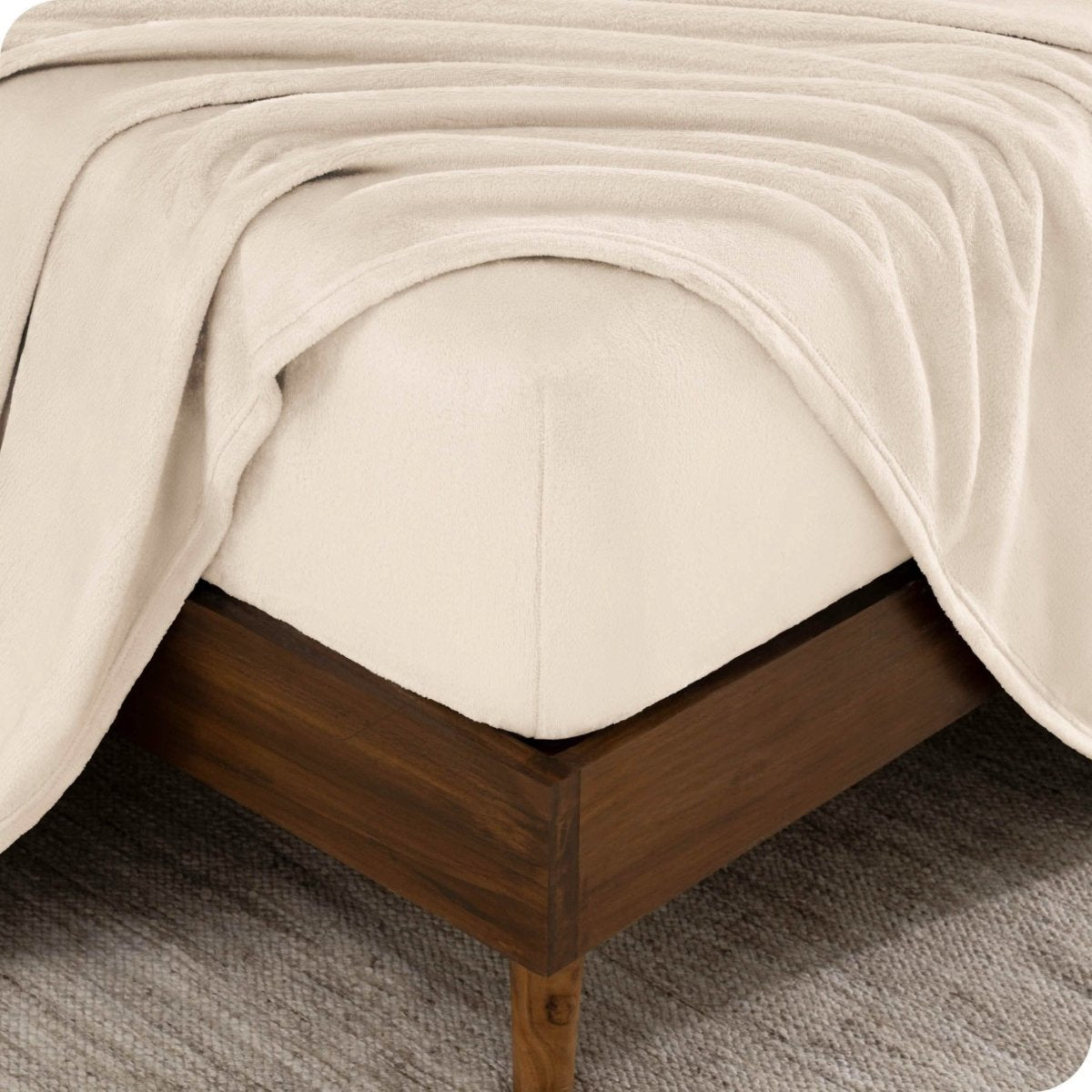 The corner of a bed frame and mattress with a fitted sheet and flat sheet on it.