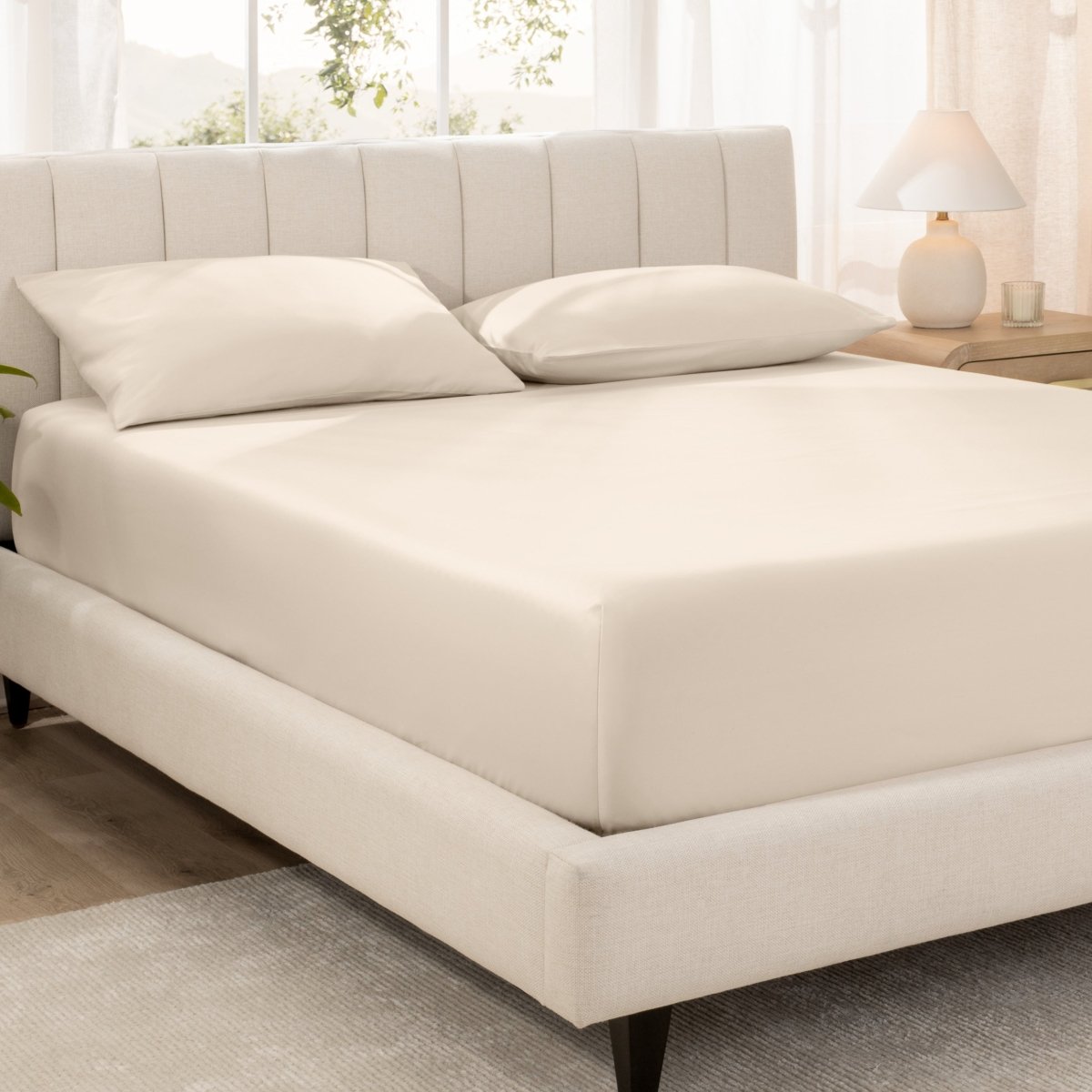 Bed with fitted sheet and pillowcases in a bright room.