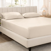 Bed with fitted sheet and pillowcases in a bright room.