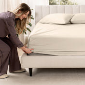 Woman adjusting a fitted sheet on a bed in a bedroom setting