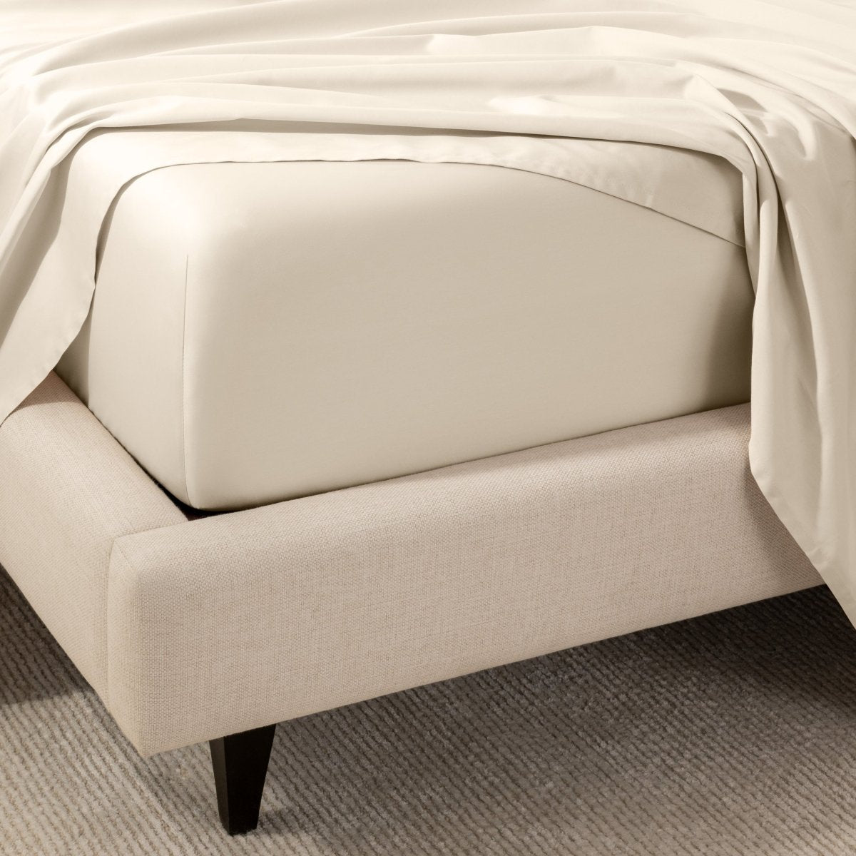 A close-up of the corner of a bed with a fitted sheet and matching flat sheet.