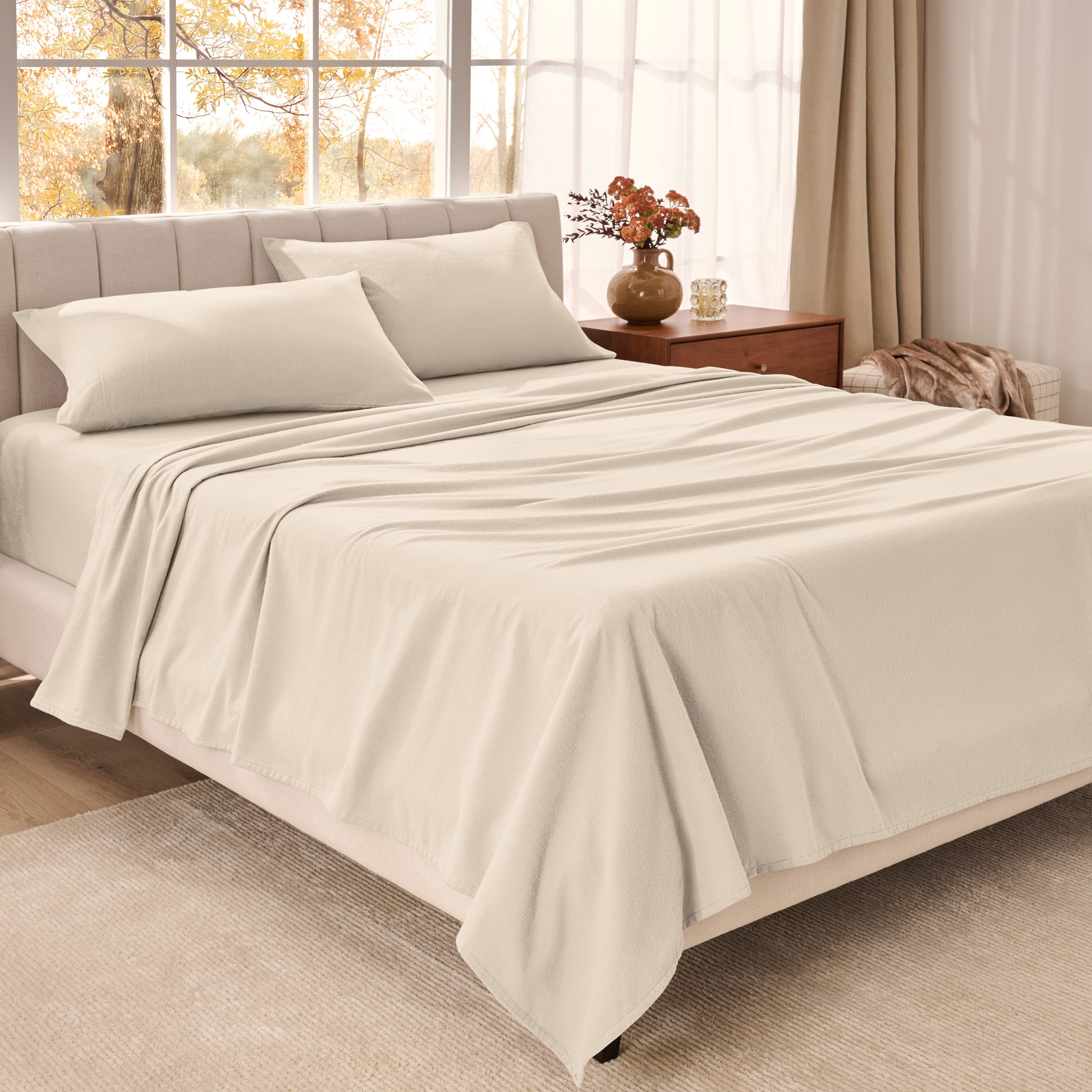 Bed sheets on a neatly made bed in a bright bedroom with large windows.