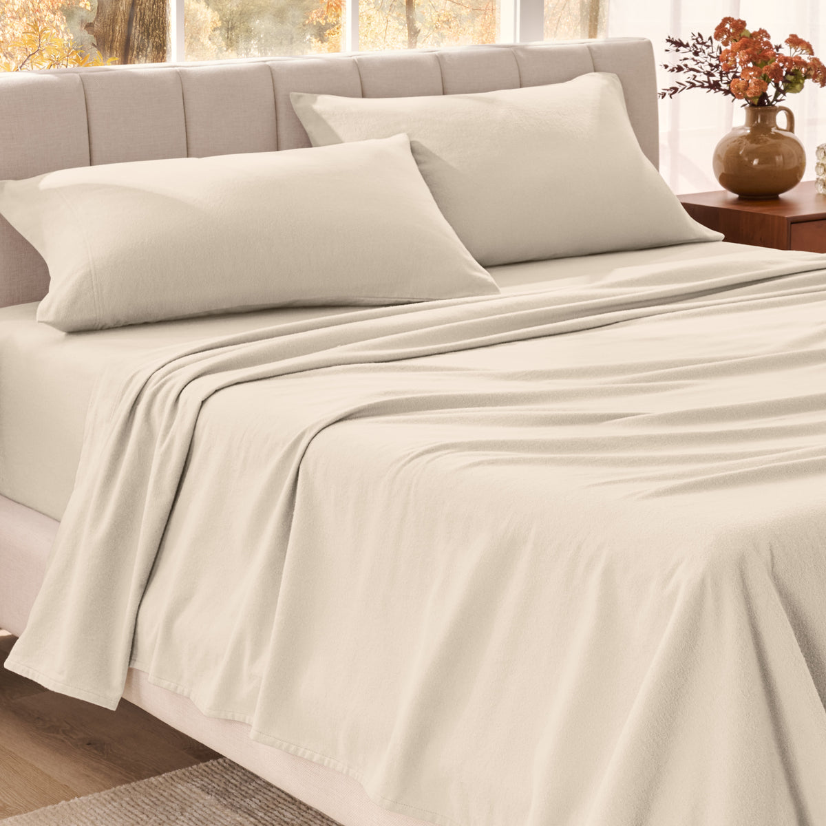 Bed sheets on a neatly made bed in a bright bedroom with large windows.