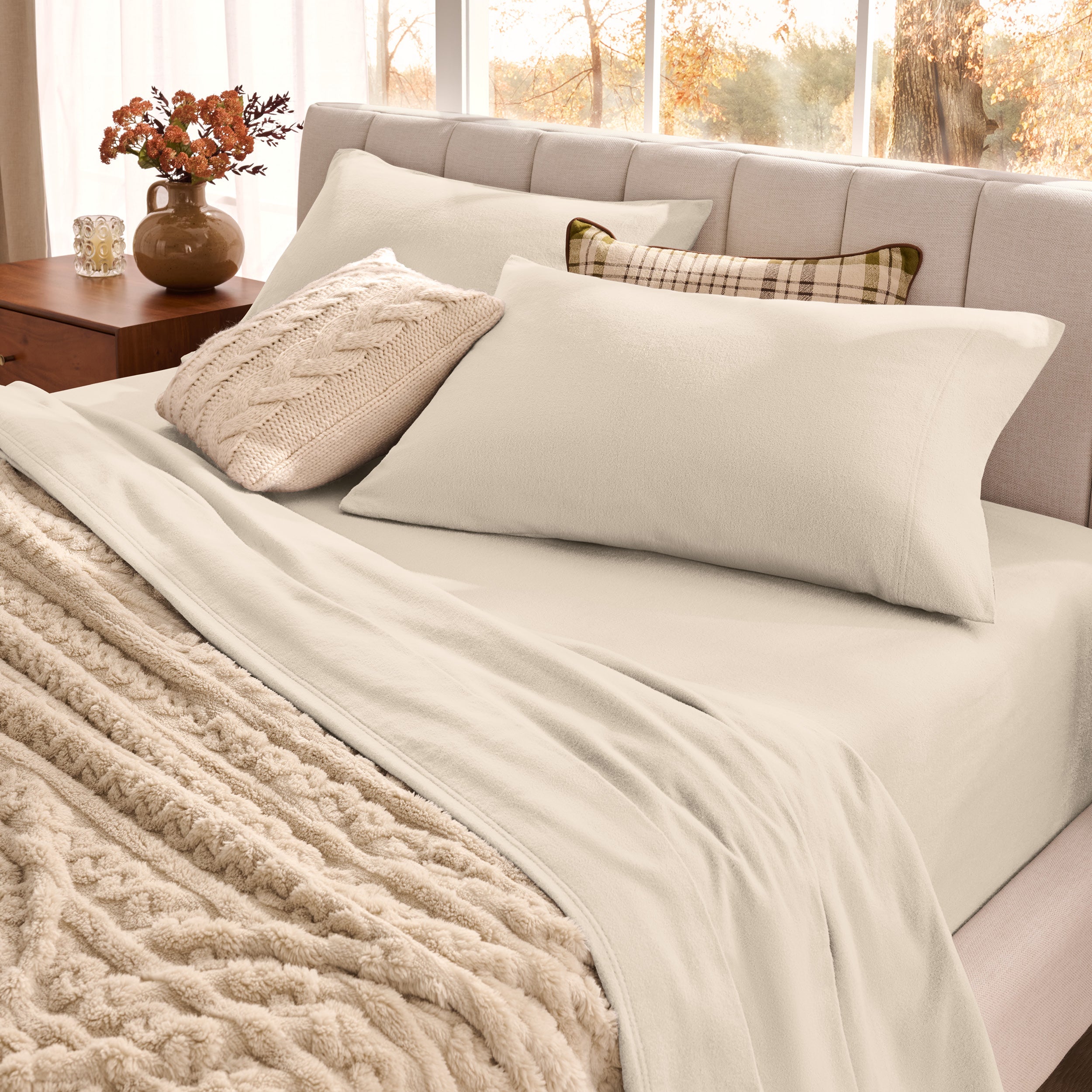 Neatly made bed with organic flannel sheets  and a beige blanket in a bright bedroom.