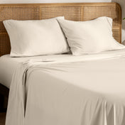 Organic jersey bed sheets and pillows on a bed with a wicker headboard.