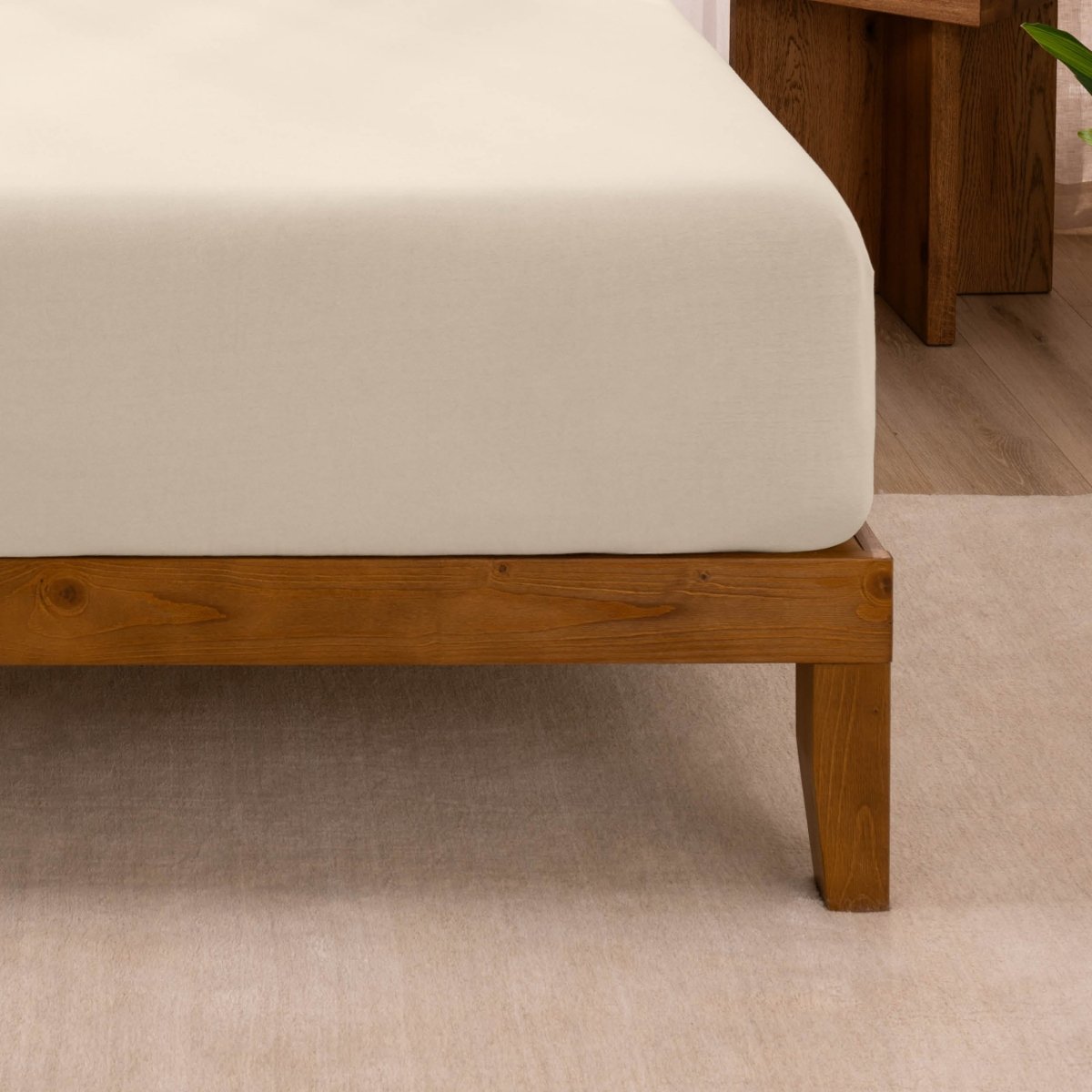 Fitted sheet on a wooden bed frame with a neutral background