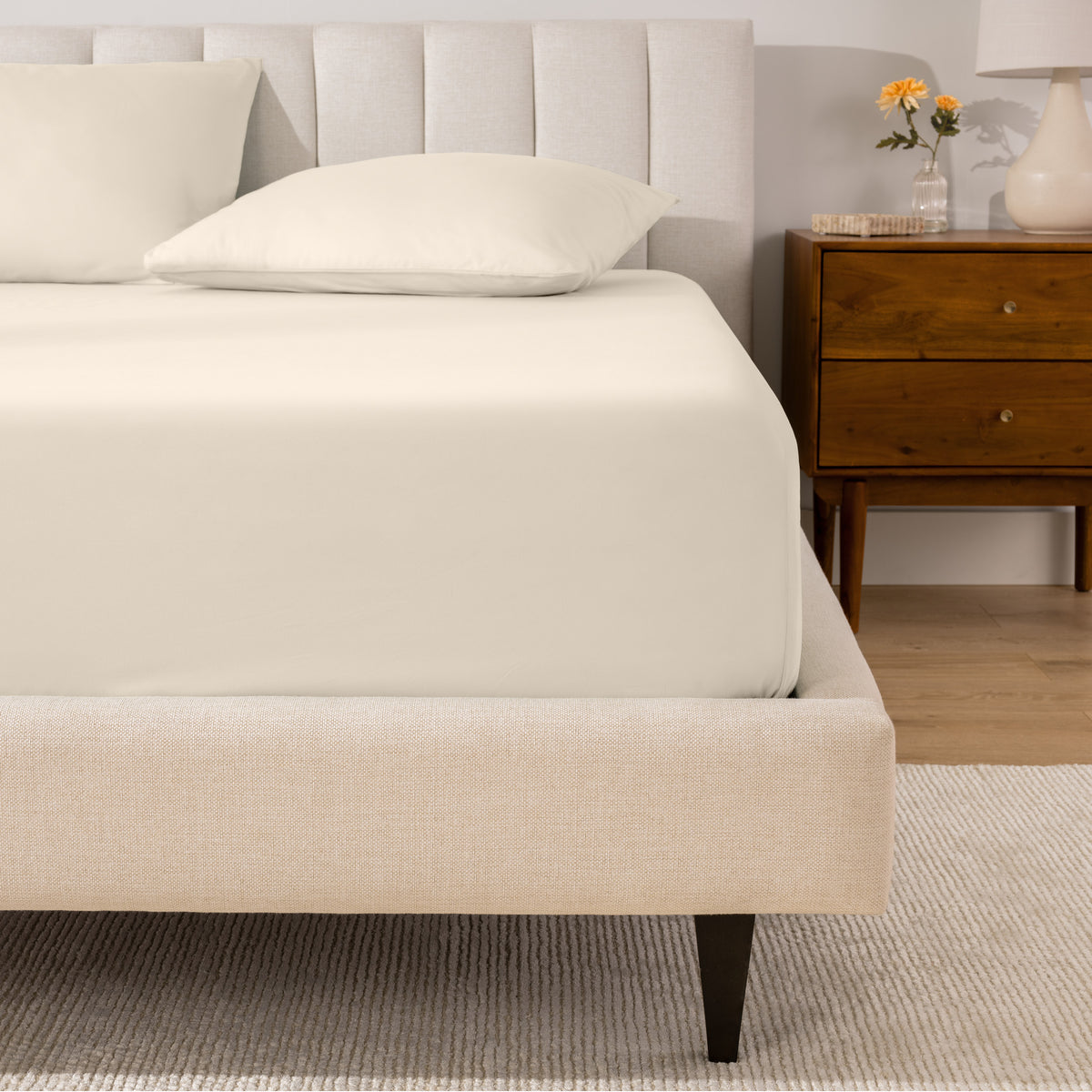 A percale fitted sheet and pillowcases on a bed in a bedroom with a wooden nightstand.