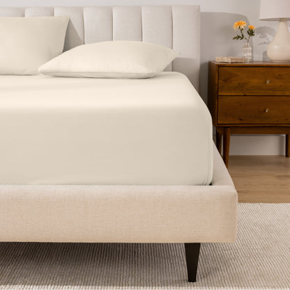 A percale fitted sheet and pillowcases on a bed in a bedroom with a wooden nightstand.