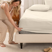 Woman in pajamas adjusting bed sheets on a bed.