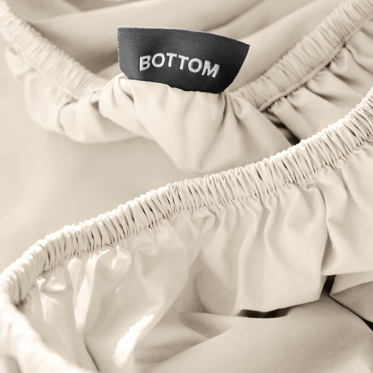 Close-up of a fitted sheet with a black fabric brand label reading BOTTOM.
