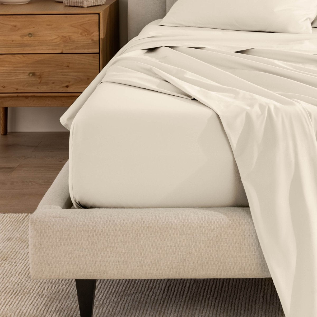 Top sheet and a matching fitted sheet on a bed with a beige bed frame