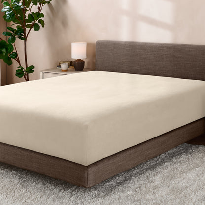 Bed with fitted sheet in a room with a lamp and plant.