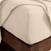 Corner of the bed with a fitted sheet on the mattress and a flat sheet draped over the side and end