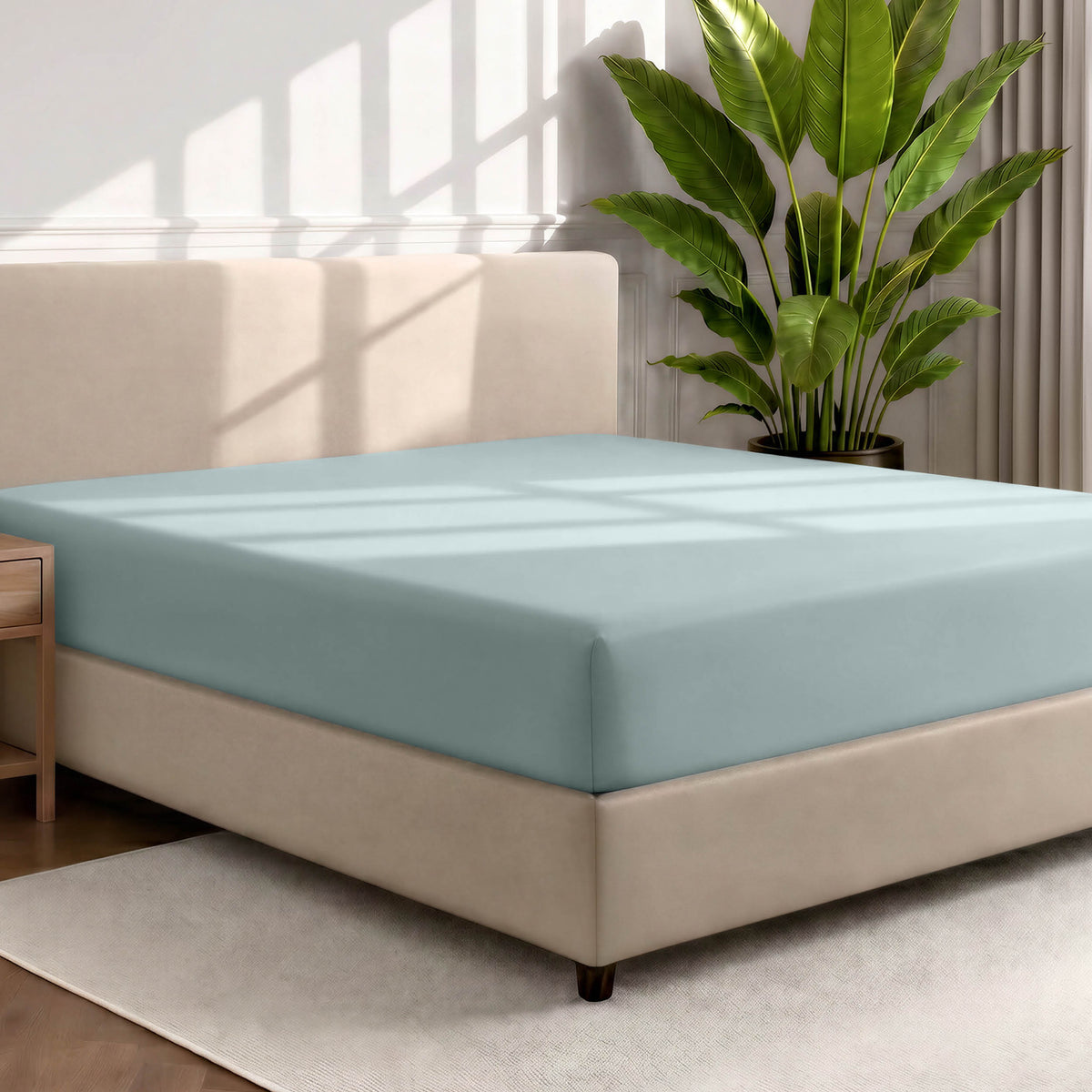 Bed with a fitted sheet in a room with a large plant and rug
