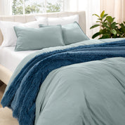Washed bedding set on a bed in a bedroom with plants and nightstands.