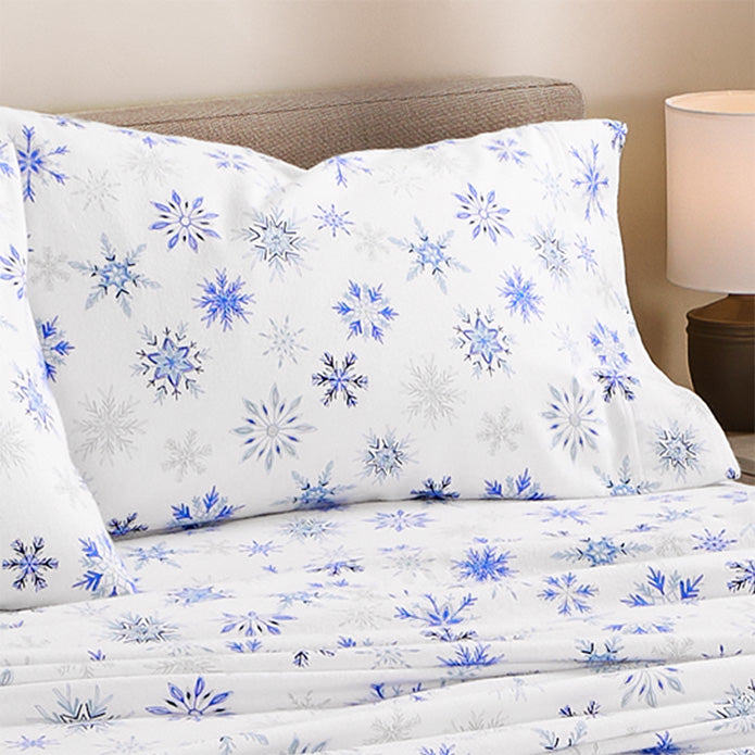 Snowflake-patterned sheet set on a bed with a lamp in the background