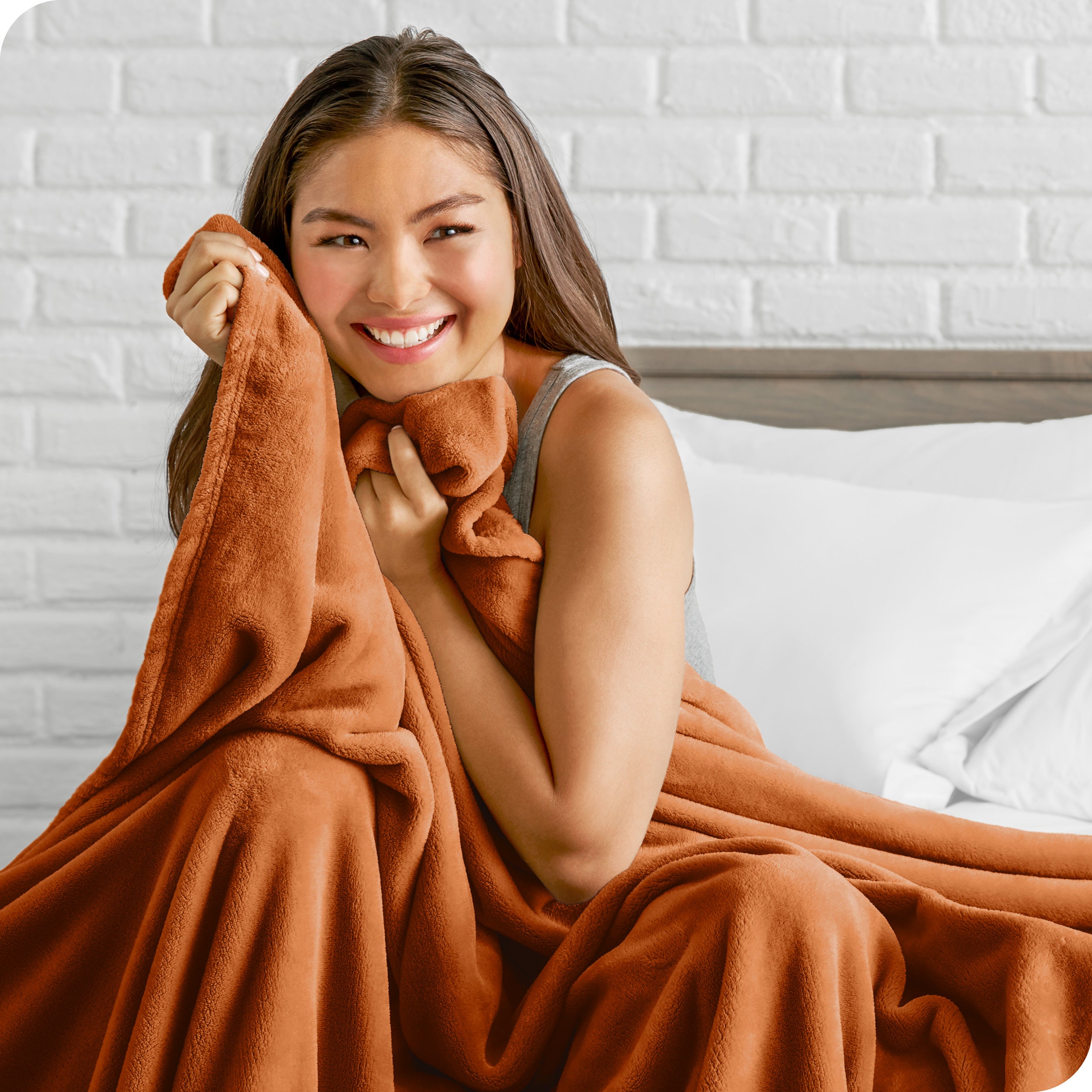 Woman sitting on a bed cuddling with a microplush blanket