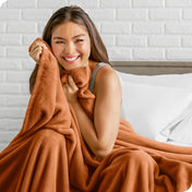 Woman sitting on a bed cuddling with a microplush blanket