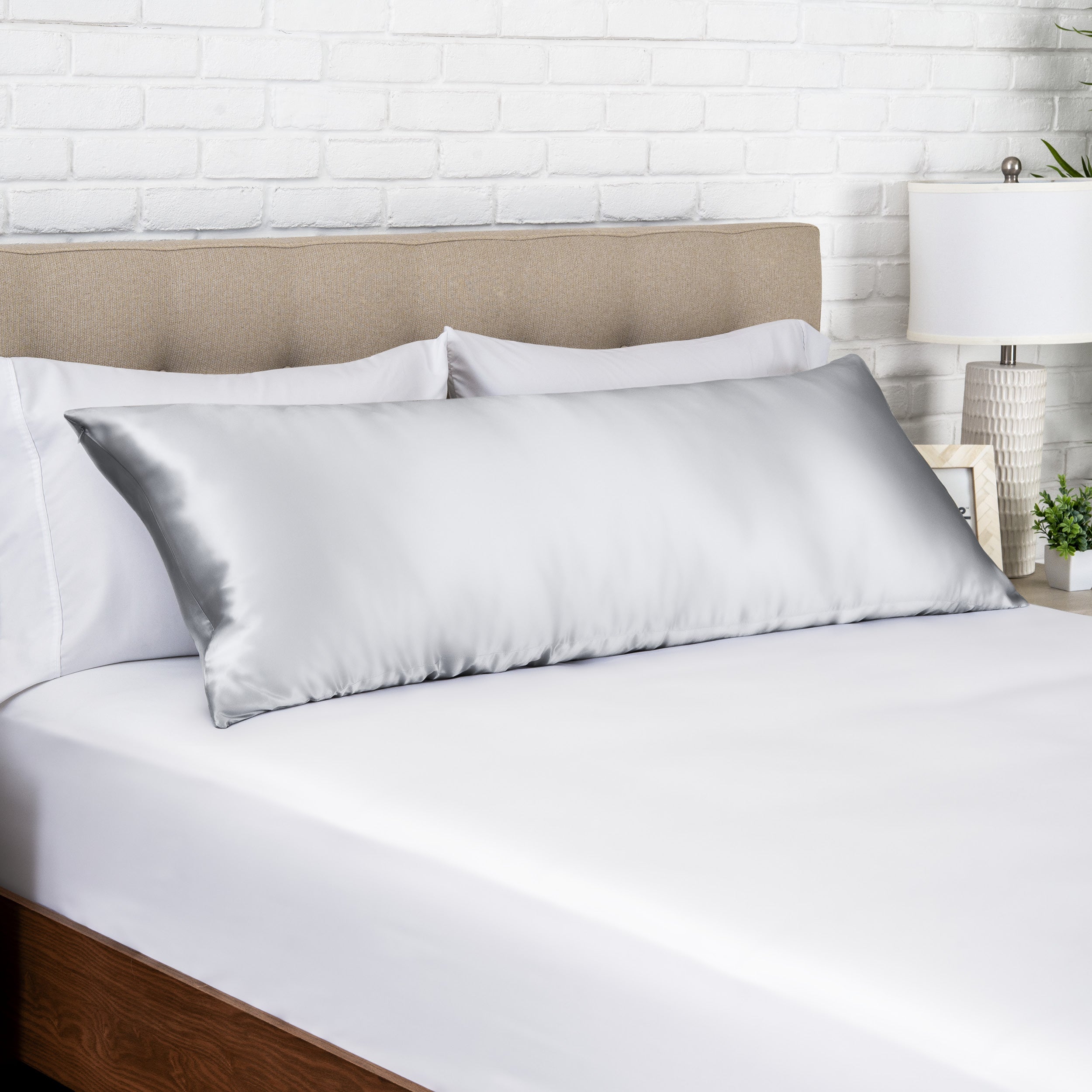 Silver silk pillow on a bed with white bedding and a beige headboard.