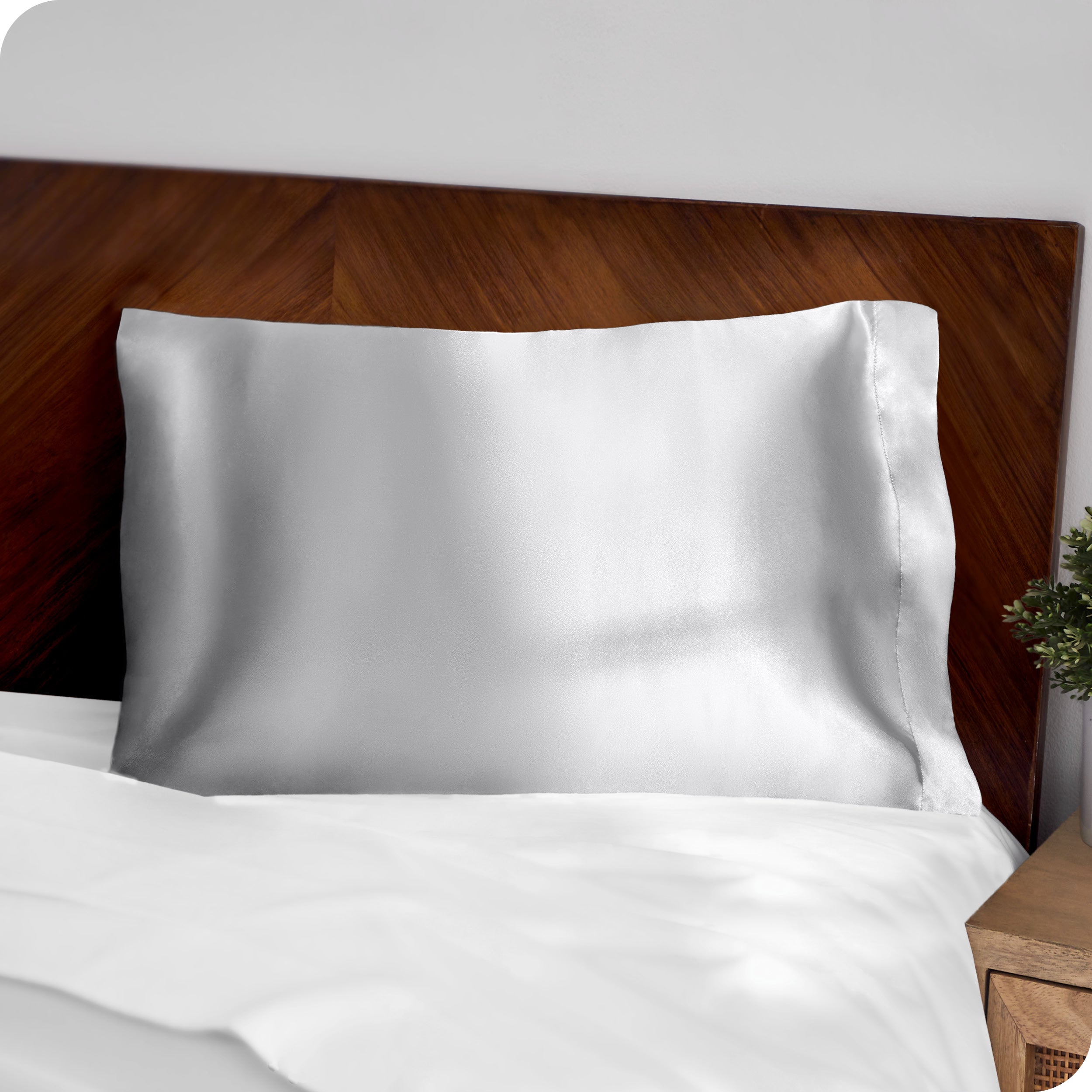 A silver silk pillowcase on a pillow resting on a headboard