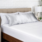 Silver satin pillow on a bed with white bedding and a wooden headboard.