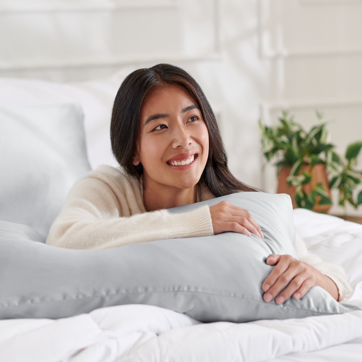 Woman lying on a bed with a body pillow, smiling.