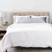 Silver satin pillow on a bed with white bedding and a wooden headboard.