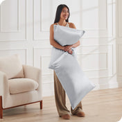 A woman has 2 pillows in her hands and they have satin pillowcases on them