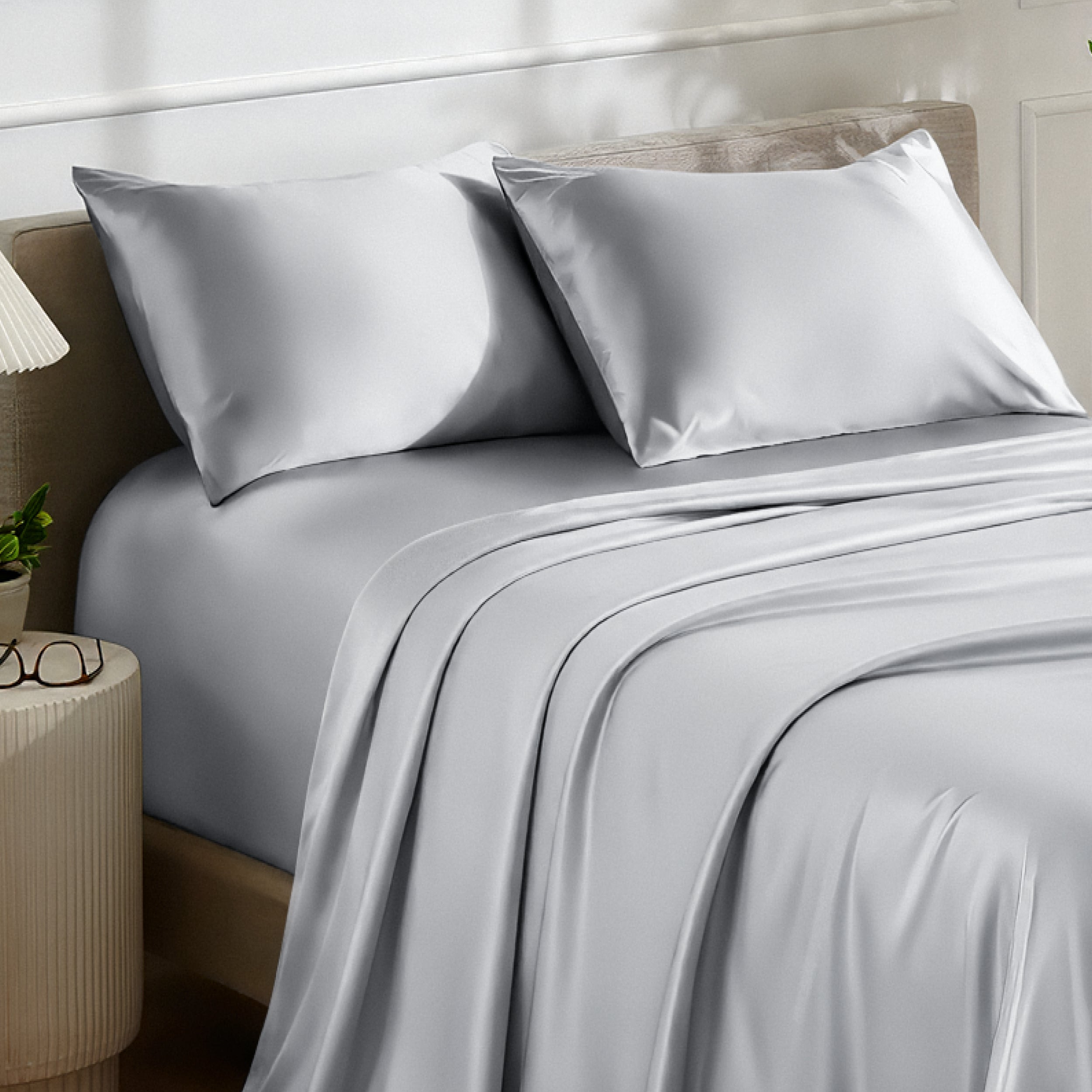Satin bedding set on a bed with a nightstand and lamp in the background.