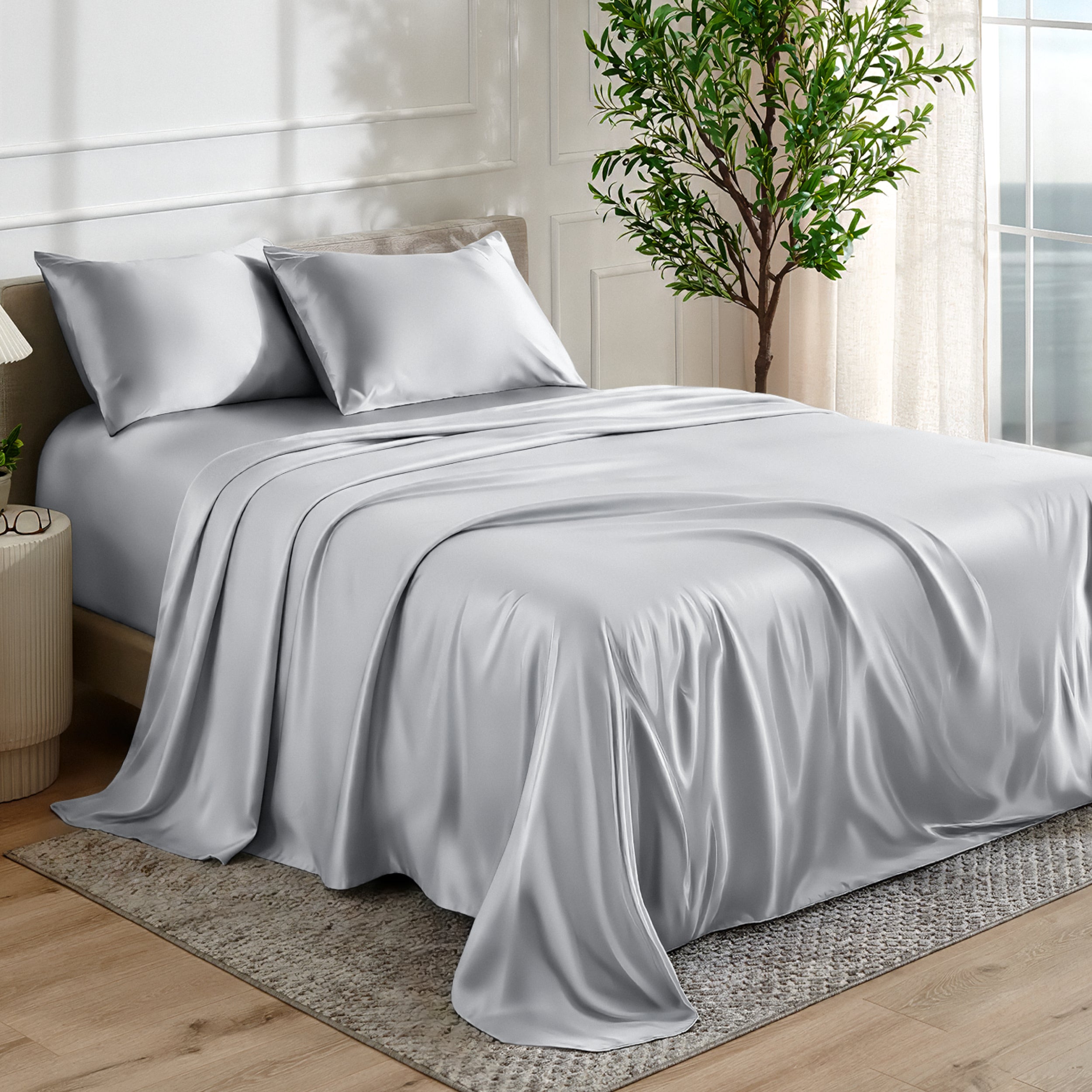 Satin sheet set on a bed in a bedroom with a plant and window in the background.
