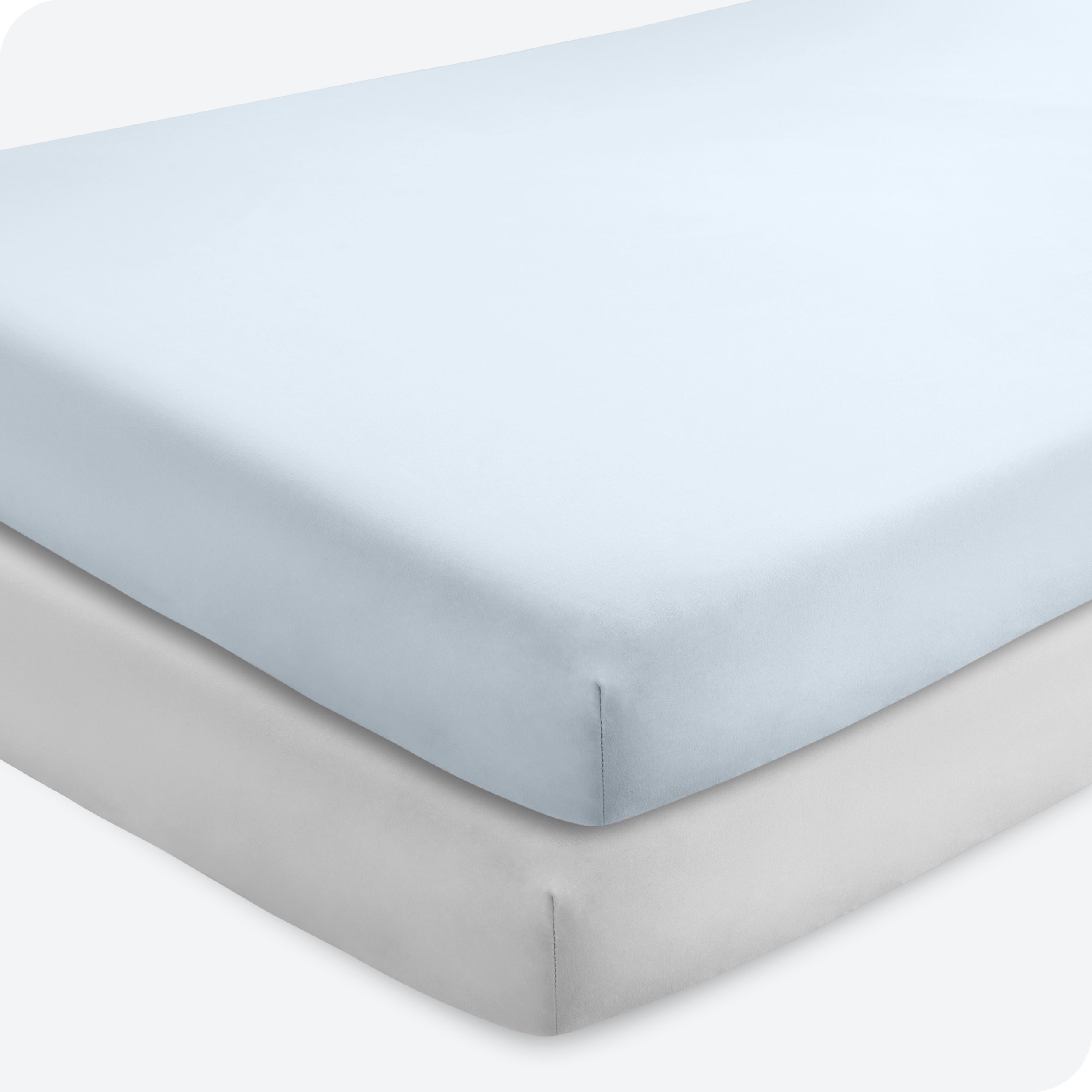 Two crib mattresses stacked with fitted sheets on them