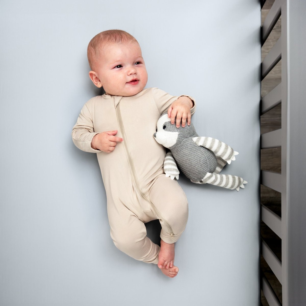 Baby in a beige onesie holding a gray and white striped toy while in a crib