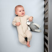 Baby in a beige onesie holding a gray and white striped toy while in a crib
