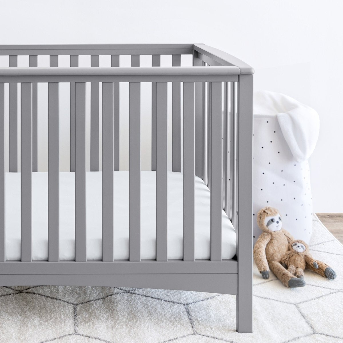 Gray crib with stuffed animals on the floor next to it