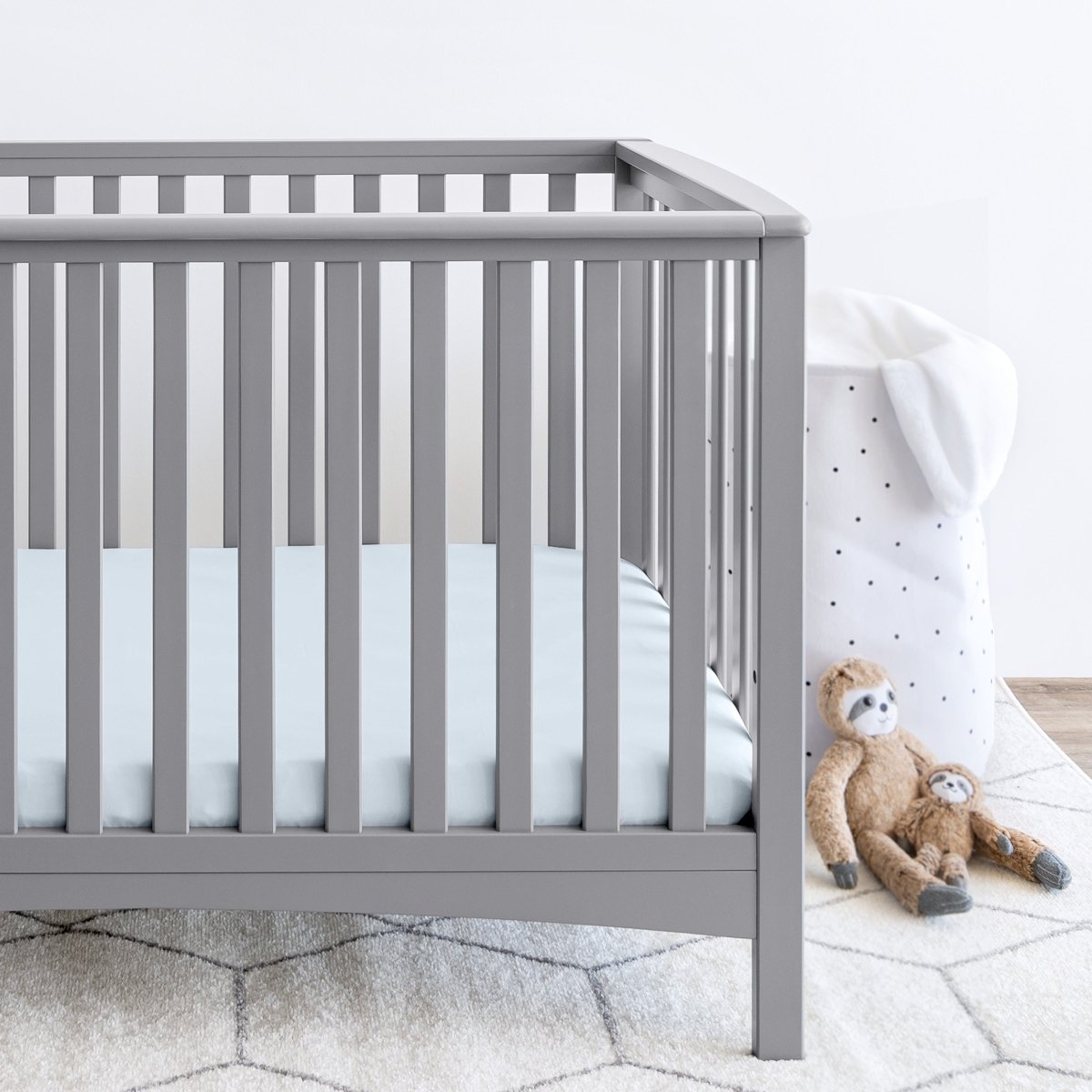 Gray crib with stuffed animals on the floor next to it