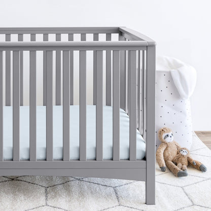 Gray crib with stuffed animals on the floor next to it