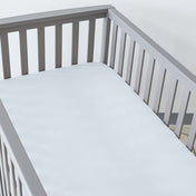 Gray crib with a fitted sheet on the mattress