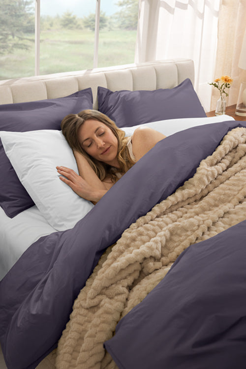 Lady sleeping on bed with white sheets and purple duvet cover