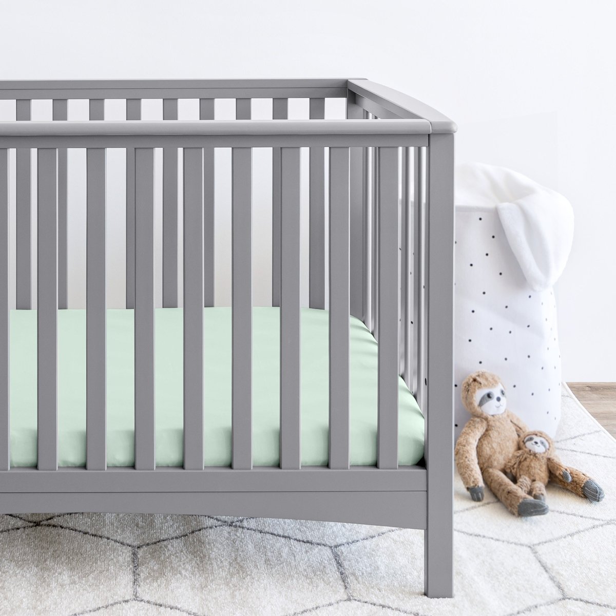 Gray crib with stuffed animals on the floor next to it