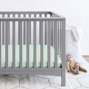 Gray crib with stuffed animals on the floor next to it