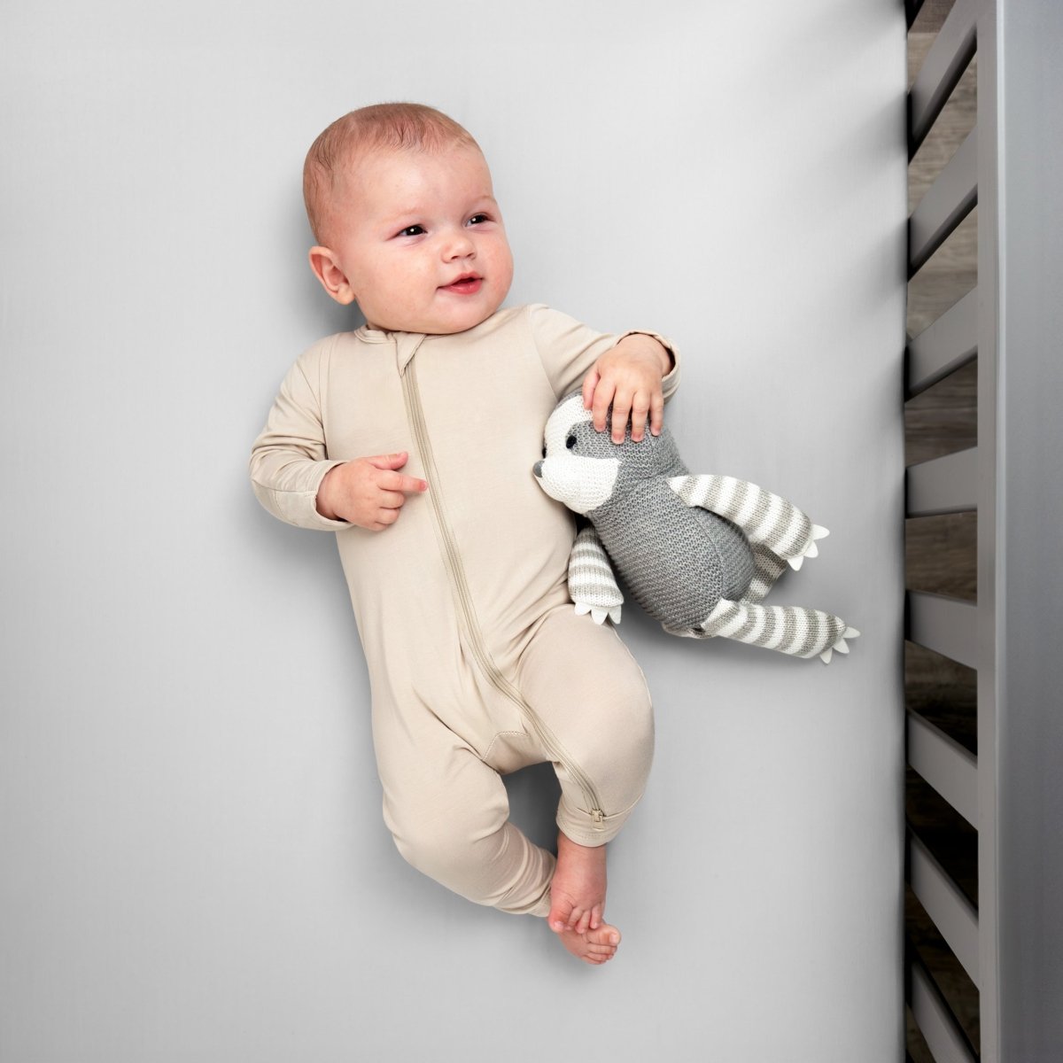 Baby in a beige onesie holding a gray and white striped toy while in a crib
