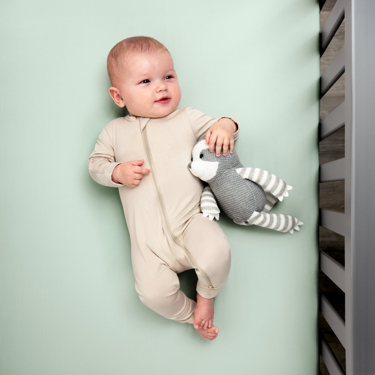 Baby in a beige onesie holding a gray and white striped toy while in a crib