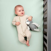 Baby in a beige onesie holding a gray and white striped toy while in a crib