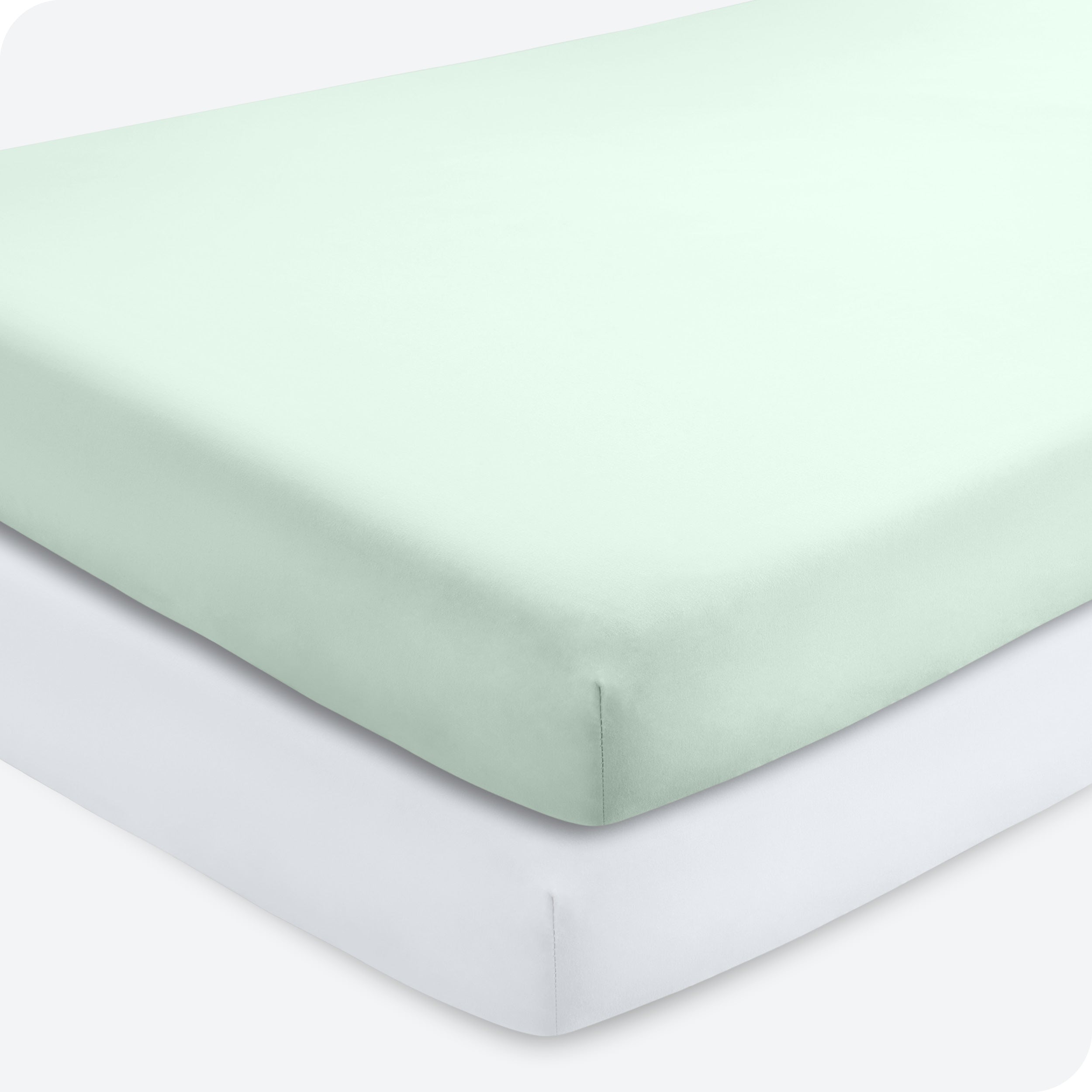Two crib mattresses stacked with fitted sheets on them