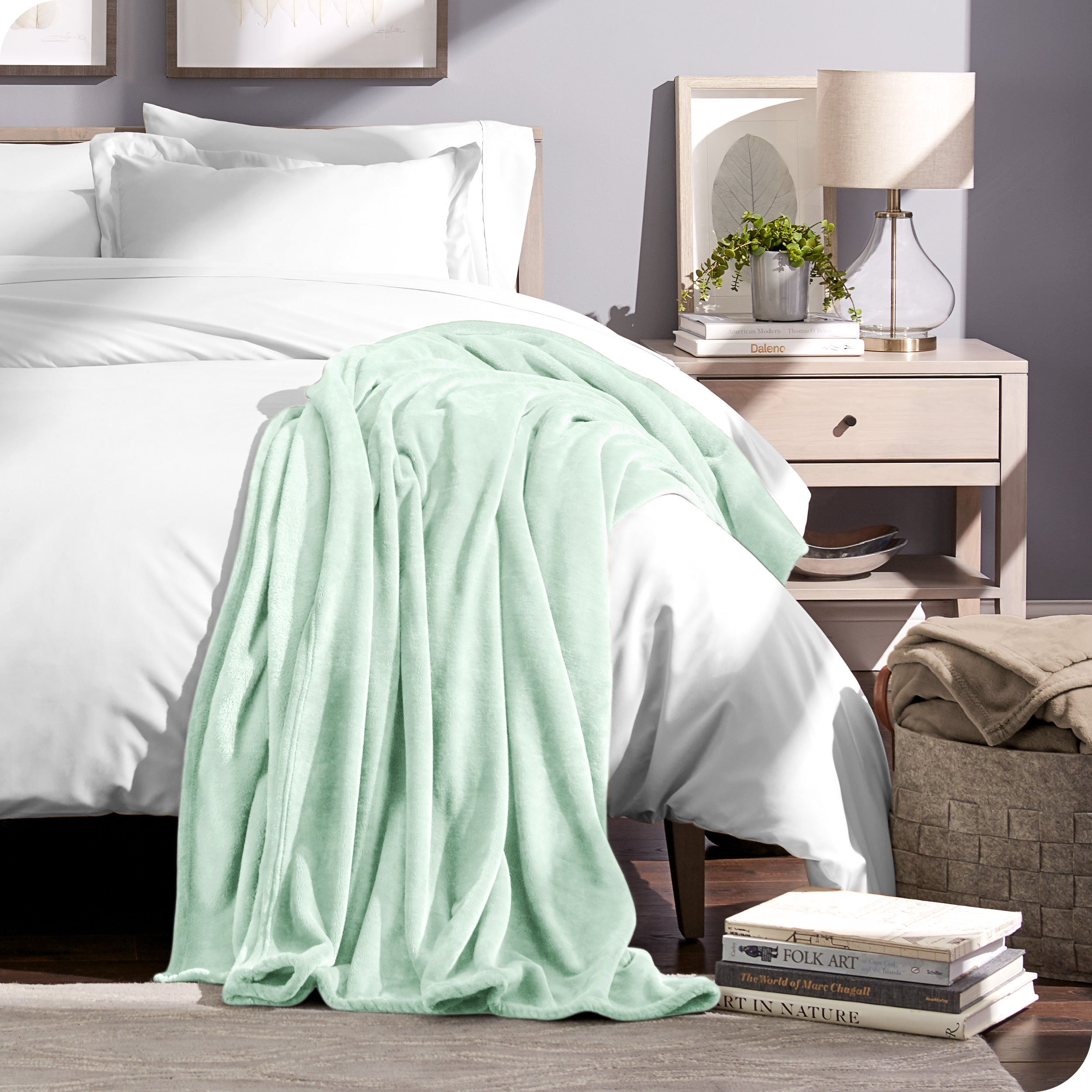 Microplush blanket draped over the end and side of a bed made with all white bedding. 