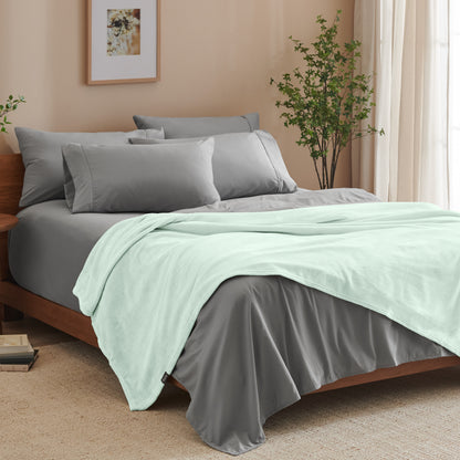 A bed made with grey sheets and a microplush blanket