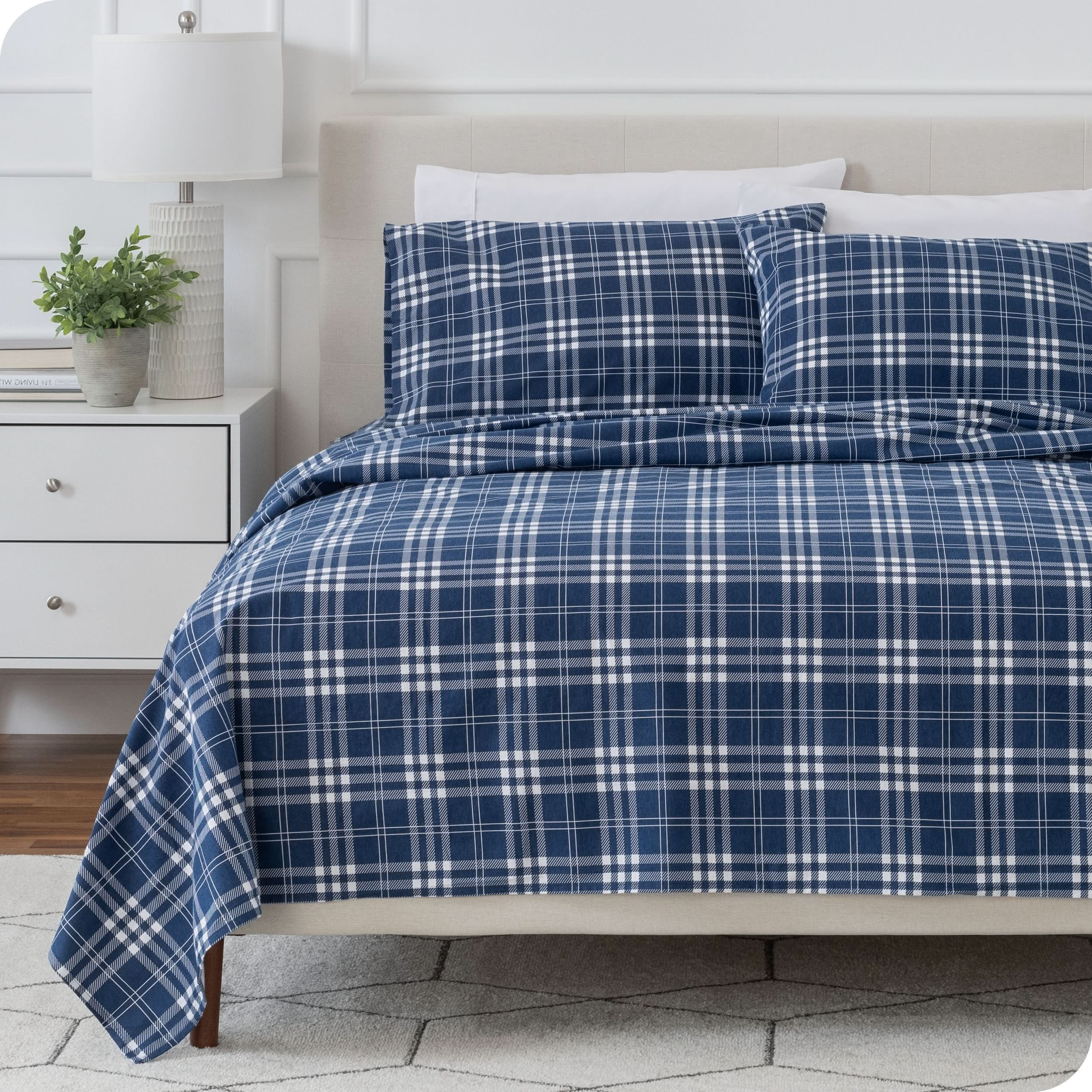 Beige bed frame with flannel print sheets on the bed