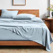 Bed with washed sheets and wooden headboard in a room setting.